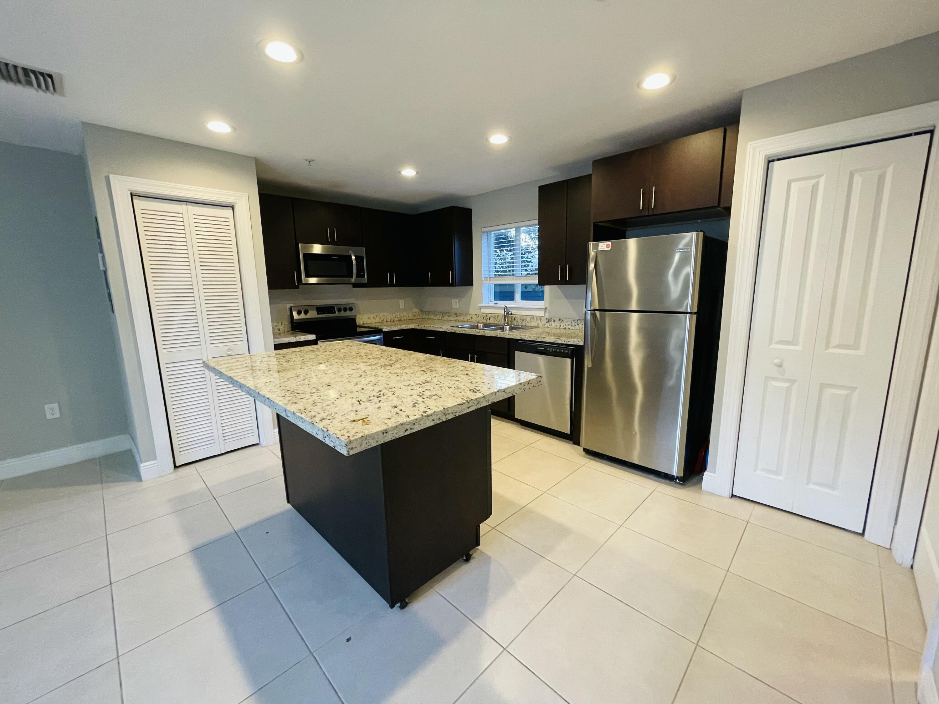 102940 Overseas Highway, Unit 2 Key Largo, FL 33037 - Photo 26 of 39 a kitchen with a refrigerator a microwave oven and a sink with wooden cabinets