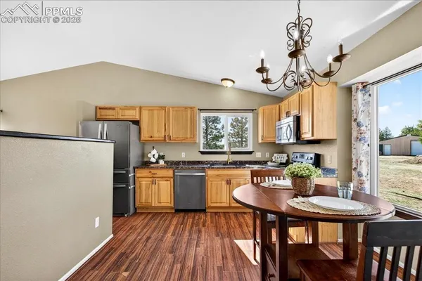 a kitchen with stainless steel appliances granite countertop a stove a refrigerator a kitchen island a dining table and chairs with wooden floor
