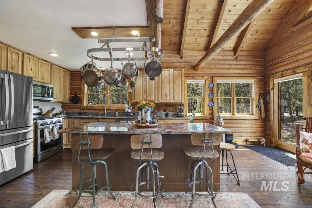 65 Goat Creek Way Stanley, ID 83278 - Photo 13 of 32 Kitchen featuring a central island with seating, a pot rack with integrated lighting, wood-finish flooring, stainless steel appliances, and exposed log wall construction