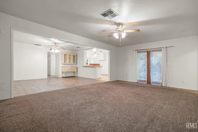 a view of an empty room with chandelier fan and windows