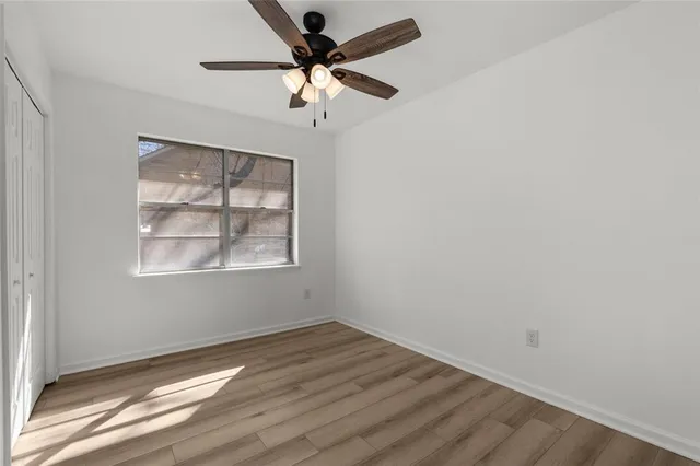 an empty room with wooden floor chandelier fan and windows