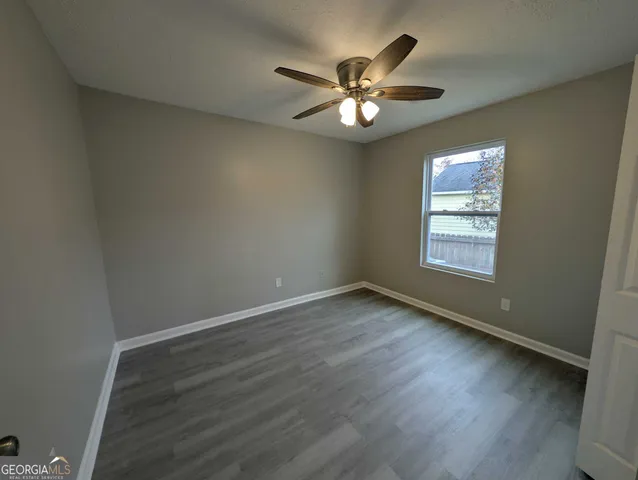 an empty room with wooden floor chandelier fan and windows