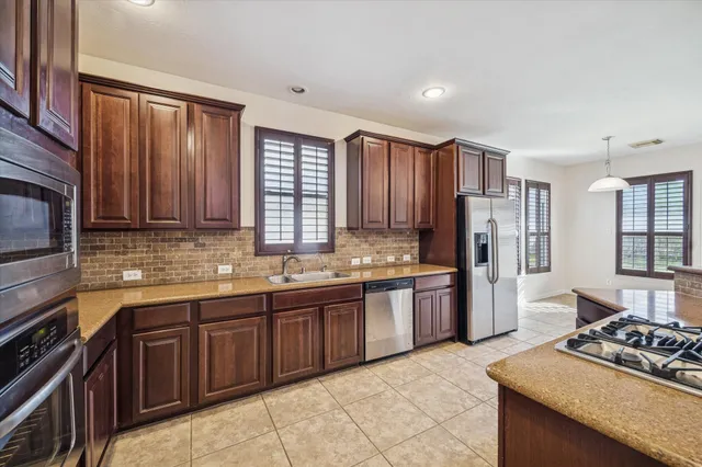 a kitchen with stainless steel appliances granite countertop wooden cabinets a sink dishwasher a stove and a refrigerator with wooden floor