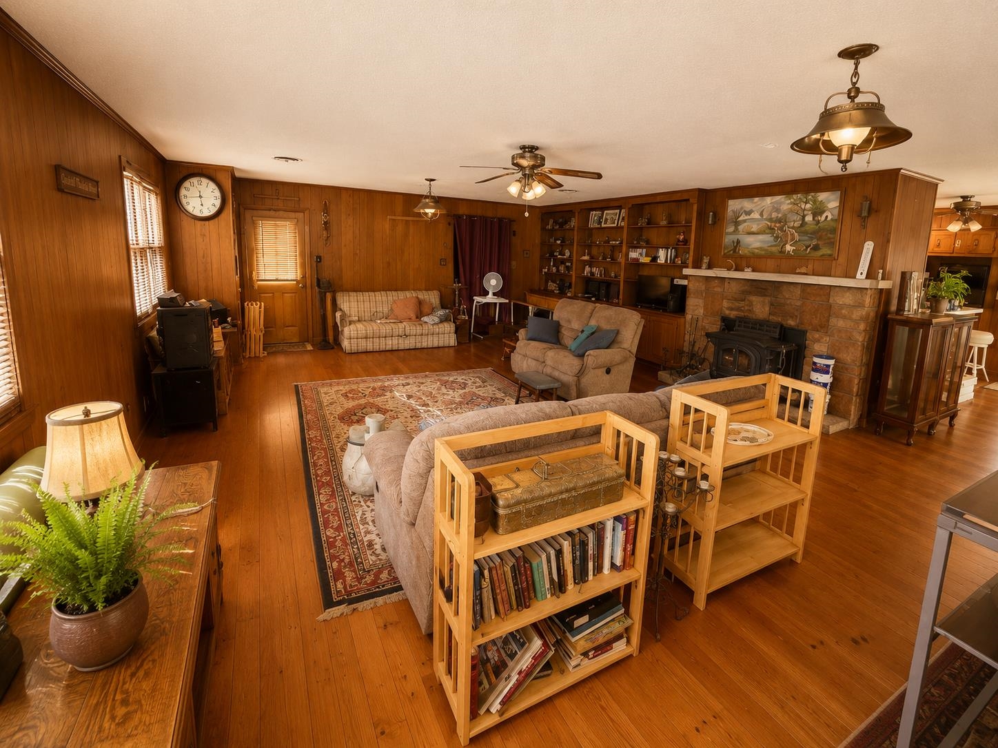 7280 Walsh Road Millington, TN 38053 - Photo 10 of 34 Living area featuring wood-finish flooring, wood paneling, multiple windows with blinds, a stone fireplace with a wood stove insert, and a built-in shelving unit