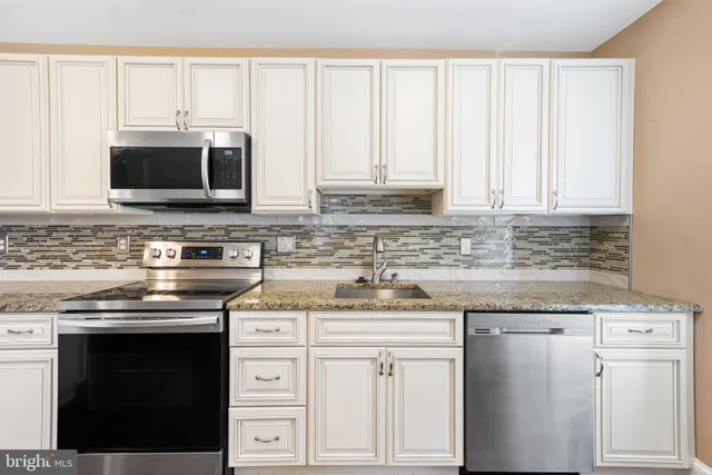 a kitchen with stainless steel appliances granite countertop a stove a sink and white cabinets
