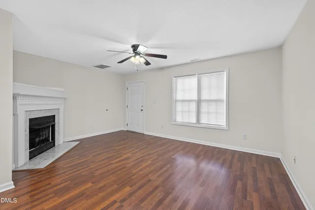 an empty room with wooden floor a ceiling fan a fireplace and windows