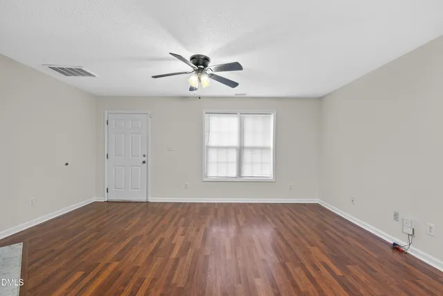 an empty room with wooden floor ceiling fan and window