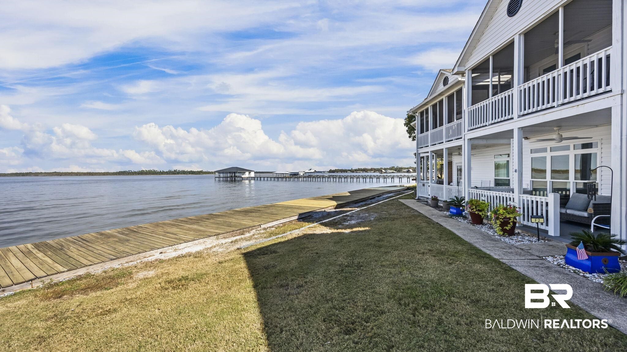 26063 Canal Road, Unit 2F Orange Beach, AL 36561 - Photo 8 of 36 View of green lawn with a water view, a boat dock, a ceiling fan, and a balcony