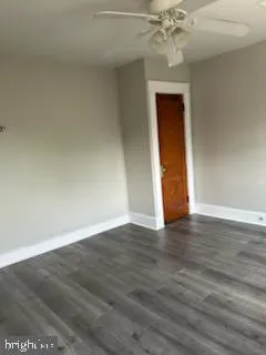 a view of an empty room with wooden floor and fan