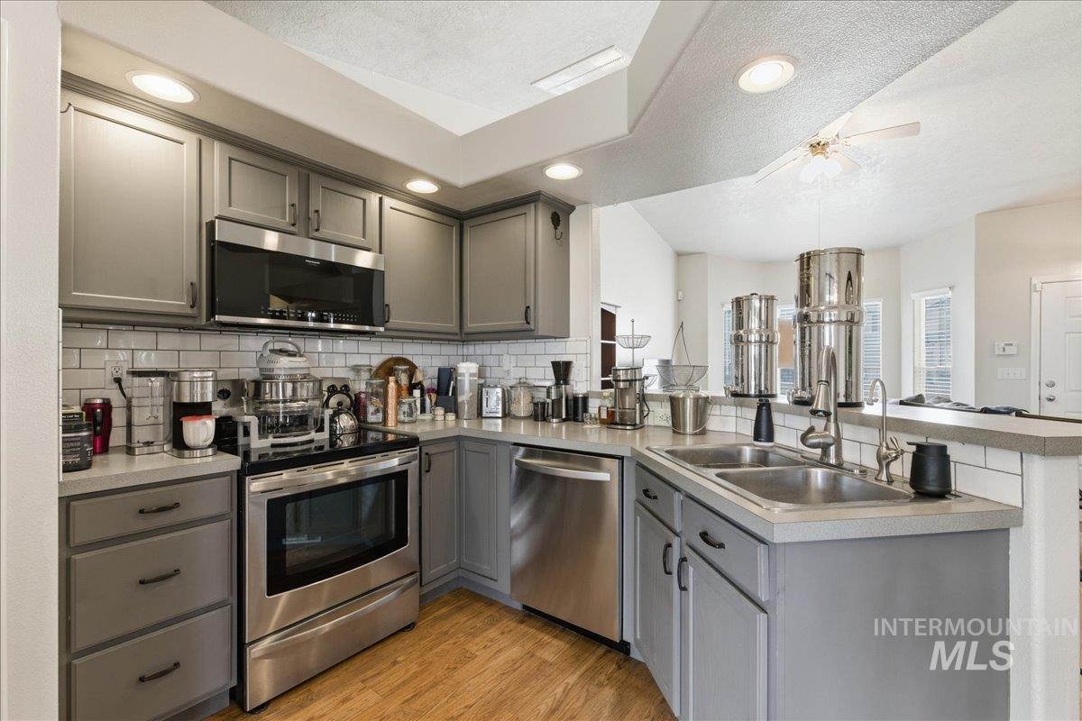 1896 West Ridge Pointe Avenue Nampa, ID 83651 - Photo 14 of 49 Kitchen with gray cabinets, a peninsula, a textured ceiling, stainless steel appliances, and light wood-style floors