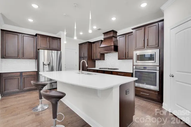 a kitchen with stainless steel appliances kitchen island granite countertop a refrigerator a stove and a sink with wooden floor