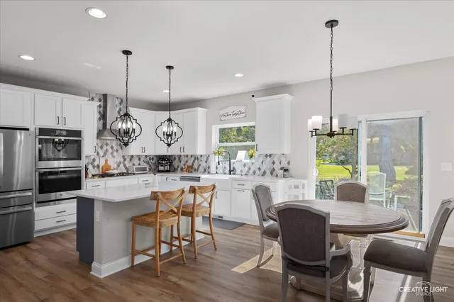 a kitchen with stainless steel appliances granite countertop a table chairs and a wooden floor