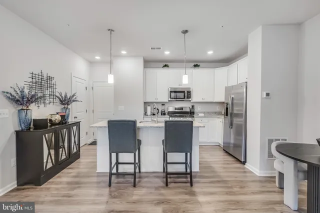 a kitchen with stainless steel appliances kitchen island granite countertop a refrigerator a stove a sink dishwasher and a dining table with wooden floor