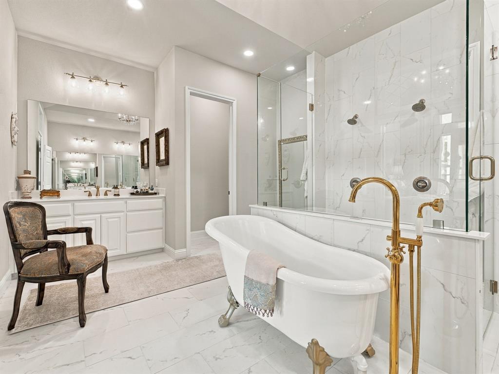 330 Rolling Bnd Road Alvord, TX 76225 - Photo 19 of 36 Freestanding tub with brass-finish floor-mounted faucet, dual shower system with glass enclosure, white marble-look tile, and dual vanity with white cabinetry