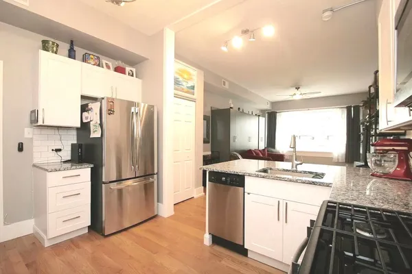 a kitchen with stainless steel appliances granite countertop a refrigerator a stove a sink and white cabinets with wooden floor