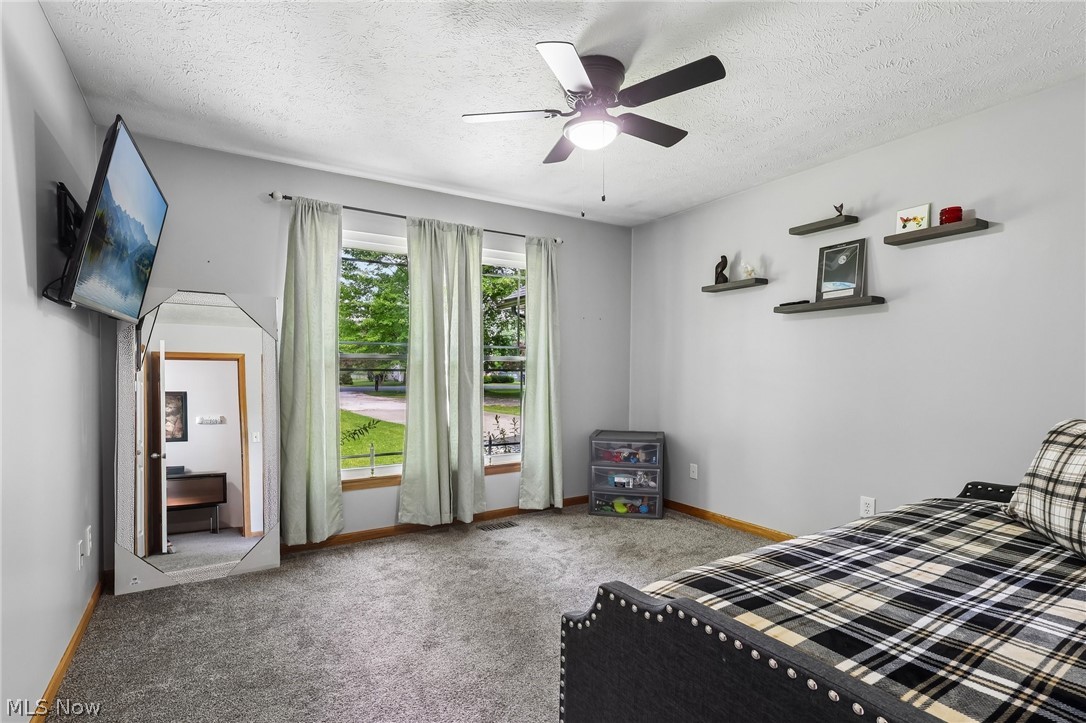 3213 Bates Road Madison, OH 44057 - Photo 26 of 45 Bright room featuring three large windows, a ceiling fan with integrated lighting, and multiple wall-mounted floating shelves