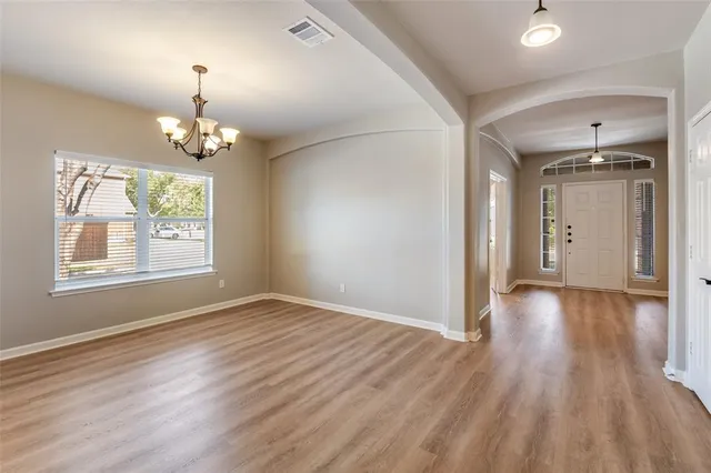 an empty room with wooden floor chandelier and windows