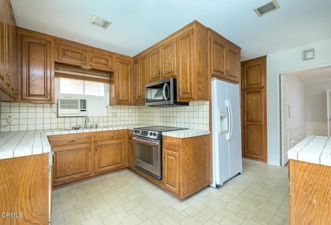 a kitchen with stainless steel appliances granite countertop wooden cabinets a stove a sink a refrigerator and a microwave