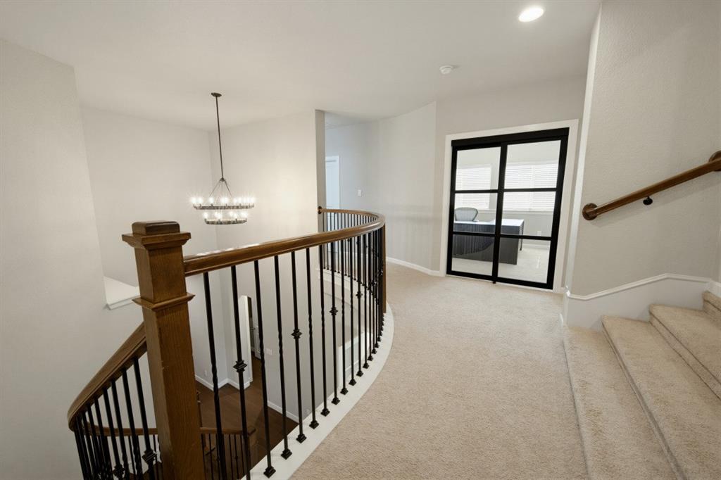 2721 Old Shire Path Road Prosper, TX 75078 - Photo 18 of 39 Upper landing featuring a curved staircase with wood banister and wrought iron spindles, a glass-paneled door, recessed lighting, and a tiered chandelier