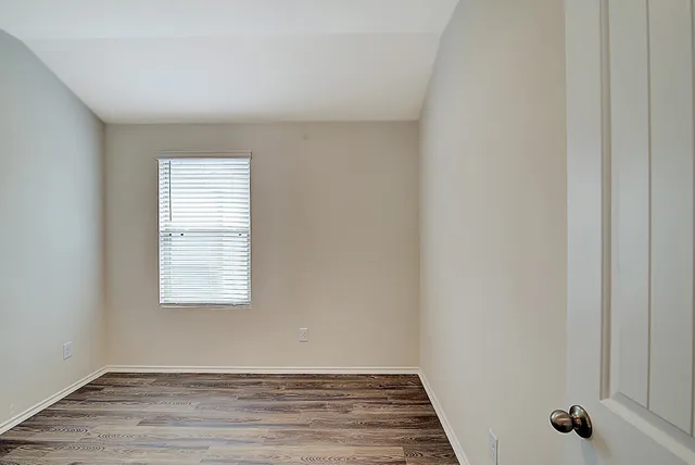 a view of an empty room with wooden floor and a window