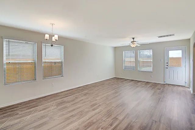 an empty room with wooden floor chandelier and windows