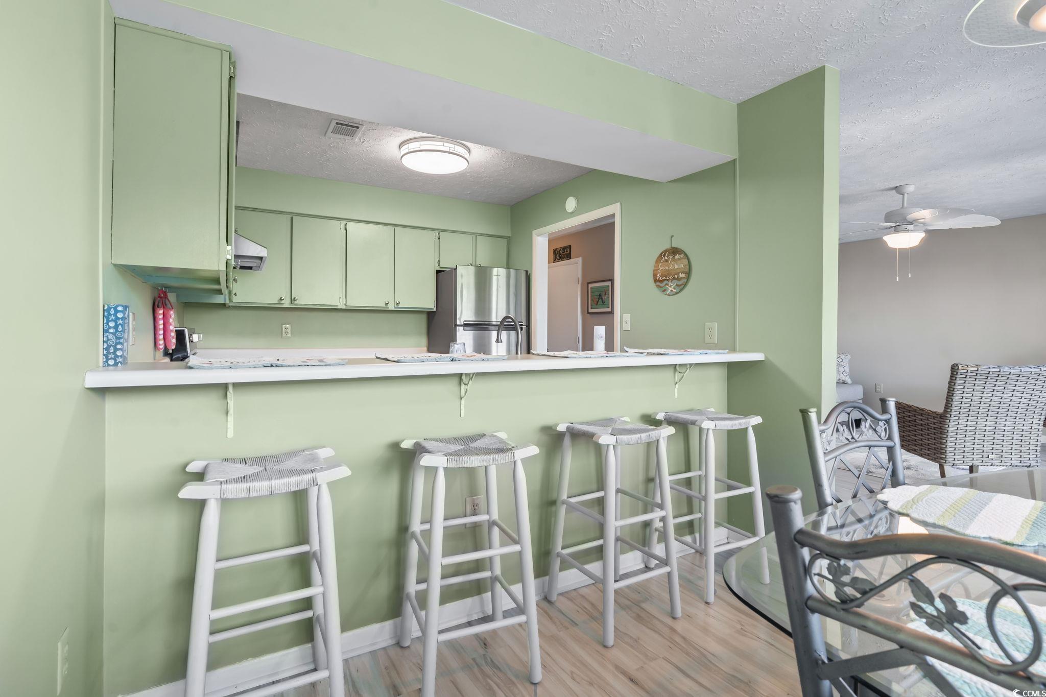 310 5th Avenue North, Unit 206 Surfside Beach, SC 29575 - Photo 7 of 40 Kitchen with a textured ceiling, light countertops, a breakfast bar area, freestanding refrigerator, and light wood-type flooring