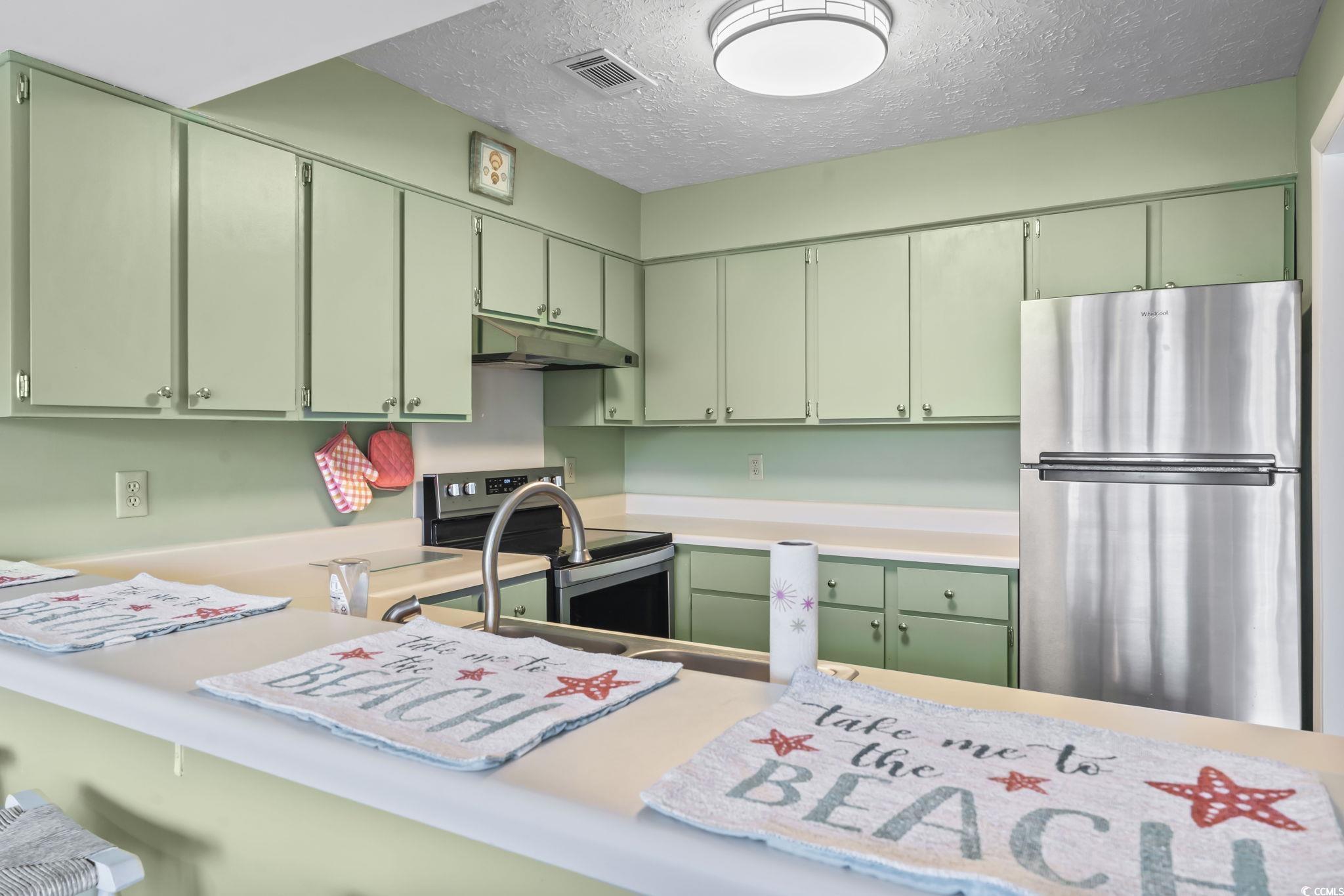 310 5th Avenue North, Unit 206 Surfside Beach, SC 29575 - Photo 8 of 40 Kitchen featuring appliances with stainless steel finishes, light countertops, green cabinets, a textured ceiling, and under cabinet range hood