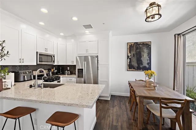 a kitchen with stainless steel appliances granite countertop a dining table chairs and refrigerator