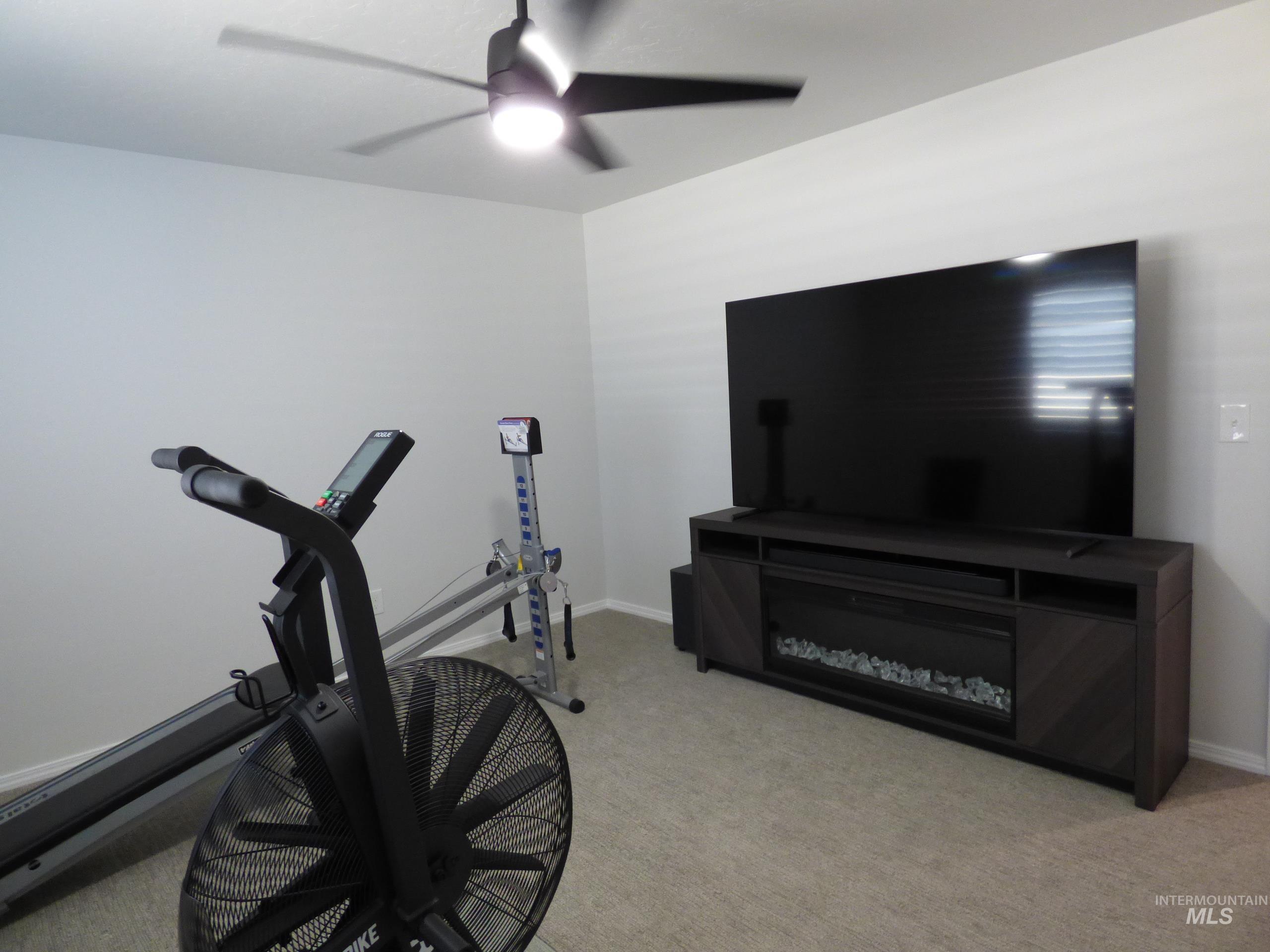 2708 East Buckaroo Drive Kuna, ID 83634 - Photo 27 of 48 Built-in media console with electric fireplace, wall-mounted television, ceiling fan with integrated lighting, and carpeted flooring