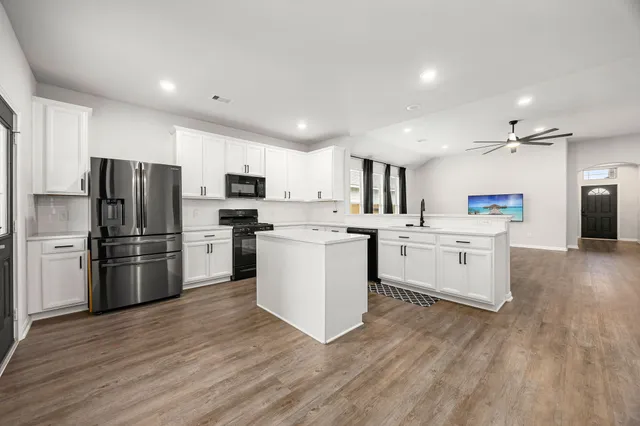 a kitchen with stainless steel appliances a sink a stove top oven a refrigerator with white cabinets and wooden floor