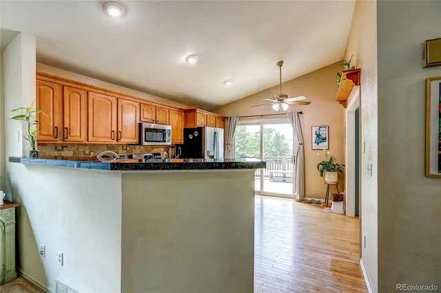 a kitchen with stainless steel appliances granite countertop a refrigerator a sink dishwasher a stove and a dining table with wooden floor