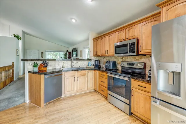 a kitchen with stainless steel appliances granite countertop a stove top oven a sink dishwasher a refrigerator and a microwave oven with wooden floor