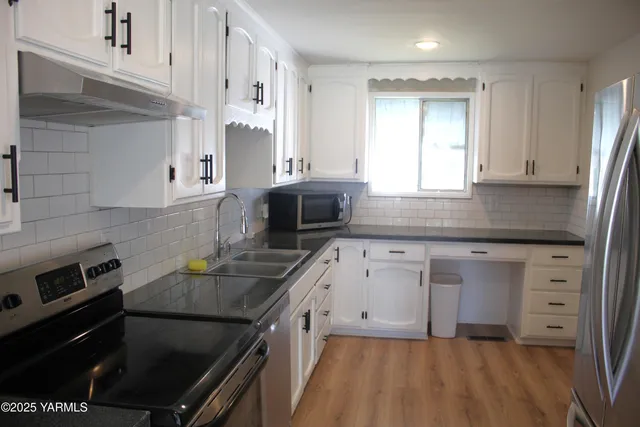 a kitchen with granite countertop a sink stainless steel appliances and white cabinets