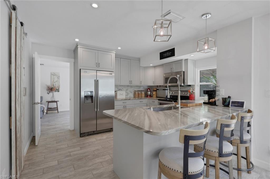 5092 Boxwood Way Naples, FL 34116 - Photo 6 of 48 Beautifully updated kitchen with Quartz countertops, Gray wood shaker cabinets, glass backsplash, newer appliances, deep kitchen sink, seating area, perfect view of the pool/patio area, and a large walk in pantry with barn door.
