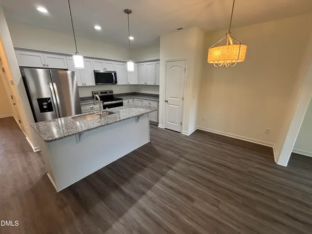 a kitchen with stainless steel appliances granite countertop a refrigerator a sink dishwasher a stove and white countertops with wooden floor