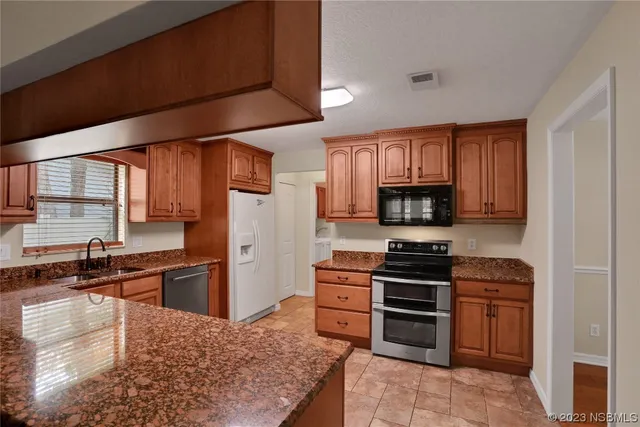 a kitchen with stainless steel appliances granite countertop a stove top oven a refrigerator a sink and dishwasher with wooden cabinets