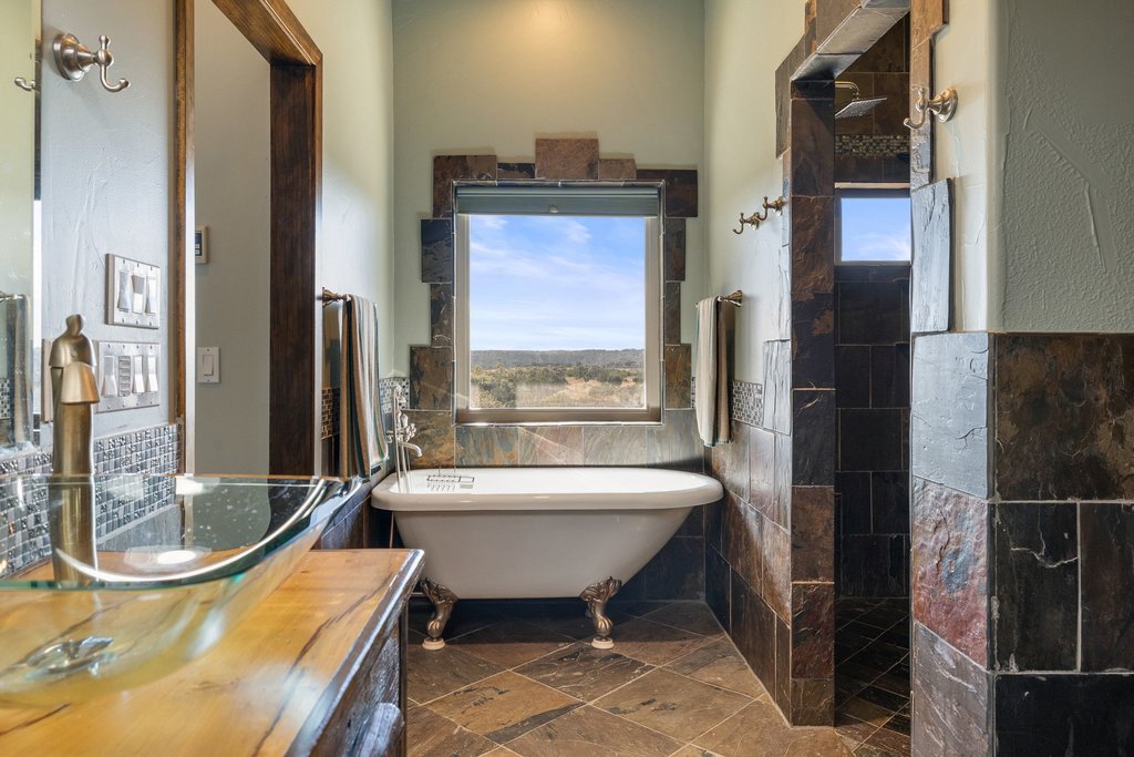1292 Upper Turtle Creek Road Kerrville, TX 78028 - Photo 16 of 40 Bathroom featuring walk in shower, a freestanding tub, vanity, a wainscoted wall, and tile walls