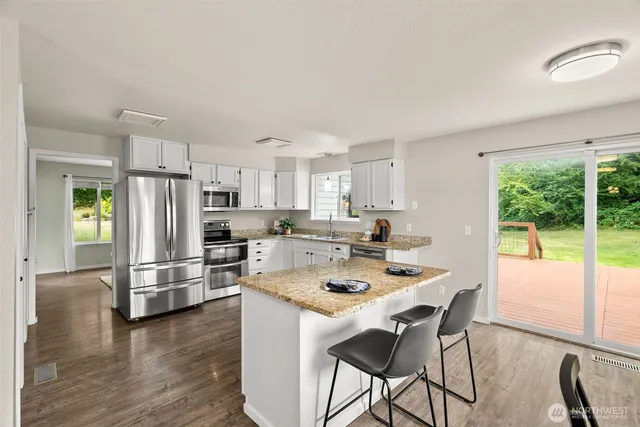 a kitchen with stainless steel appliances granite countertop a stove a refrigerator a sink a dining table and chairs with wooden floor