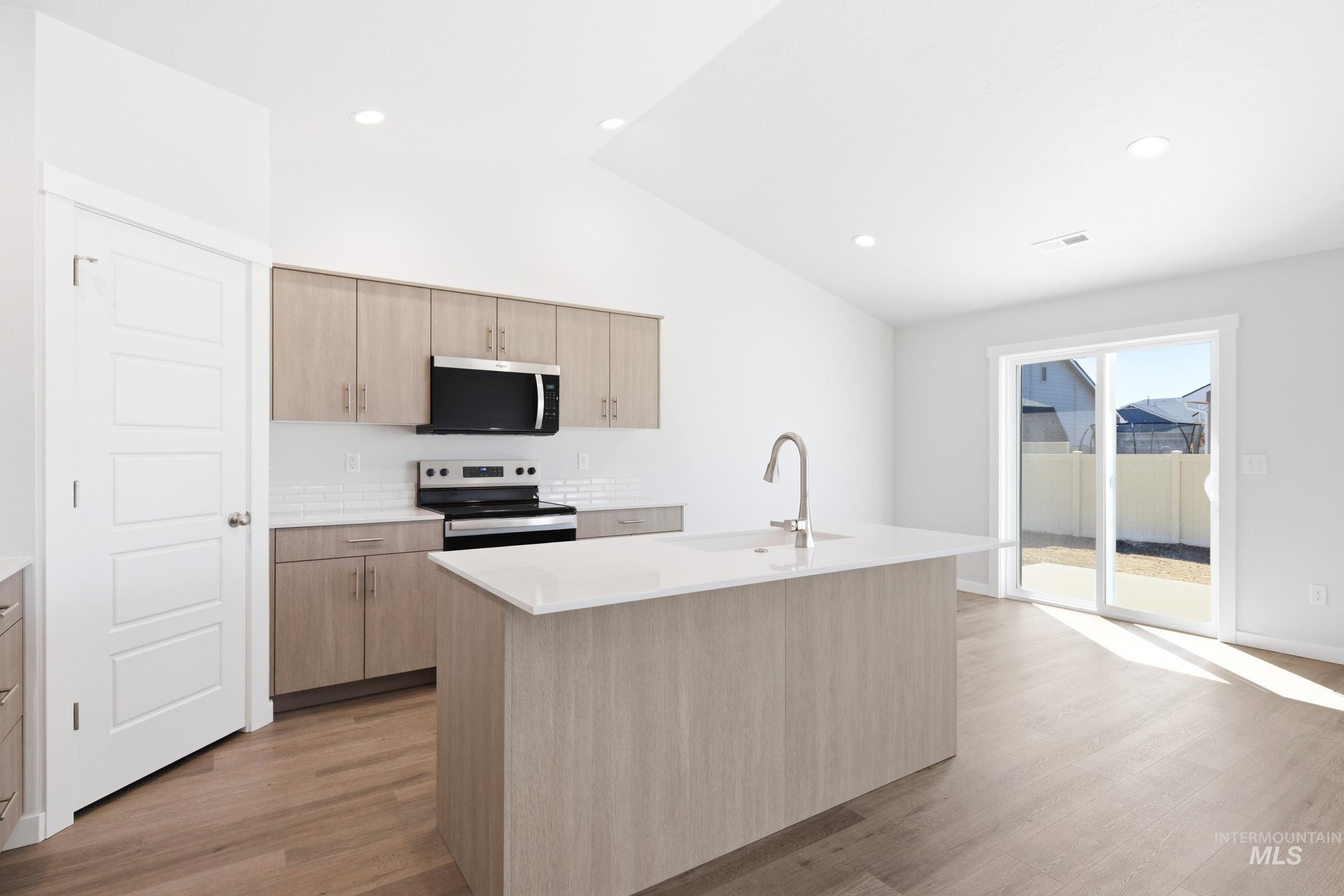 12877 Decatur Street Nampa, ID 83651 - Photo 4 of 22 Open-concept kitchen featuring an island with a sink and modern faucet, light wood-finish cabinetry, stainless steel appliances, and a white subway tile backsplash