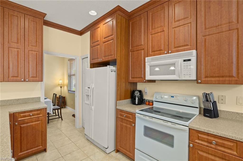 1409 Athol Way, Unit 101 Naples, FL 34104 - Photo 11 of 37 Kitchen featuring light tile patterned floors, brown cabinets, and white appliances