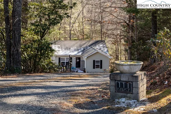 a view of a white house with a large tree and plants