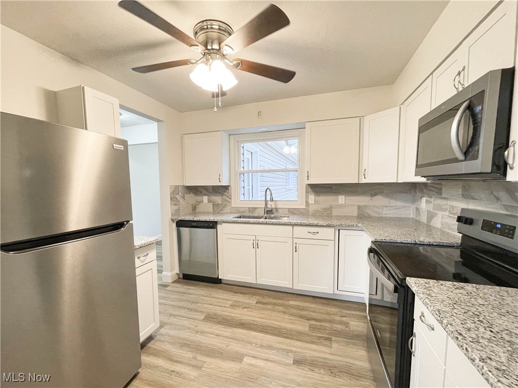 4949 East Radio Road Youngstown, OH 44515 - Photo 8 of 37 Kitchen featuring white cabinets, decorative backsplash, stainless steel appliances, and light hardwood / wood-style floors