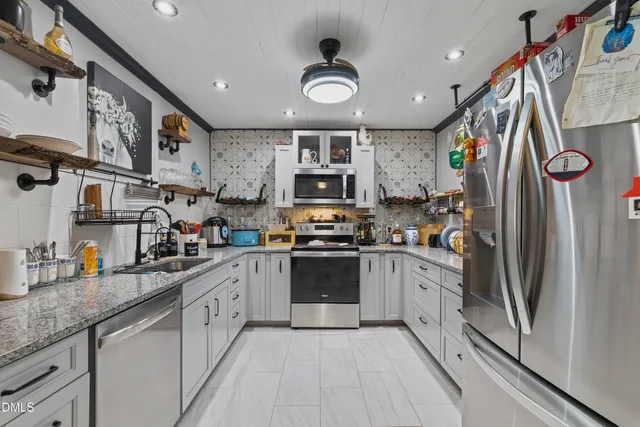 a kitchen with stainless steel appliances granite countertop a refrigerator a sink dishwasher a stove and white cabinets with wooden floor