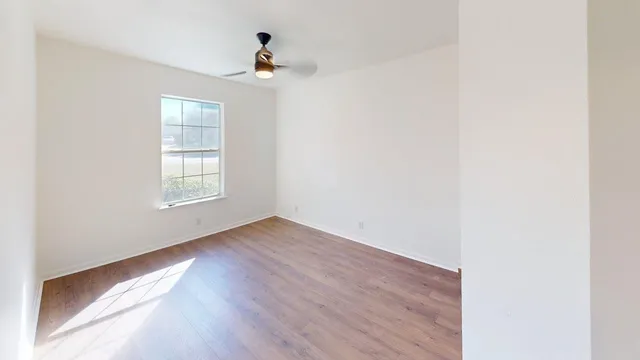 a view of an empty room with wooden floor and a window