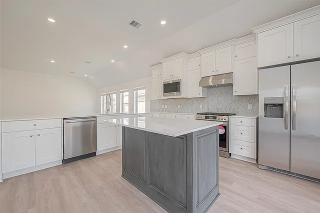 a large kitchen with stainless steel appliances granite countertop a stove a sink a refrigerator and white cabinets with wooden floor