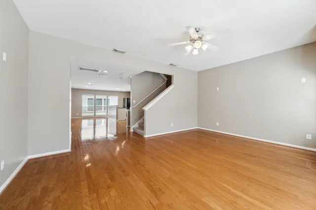 a view of an empty room with wooden floor and a ceiling fan