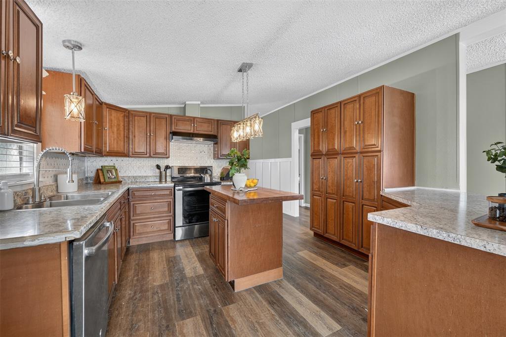 449 Big Salty Lane Springtown, TX 76082 - Photo 8 of 25 Kitchen featuring wood-finish flooring, ample wood cabinetry, granite-style countertops, stainless steel appliances, and a central island