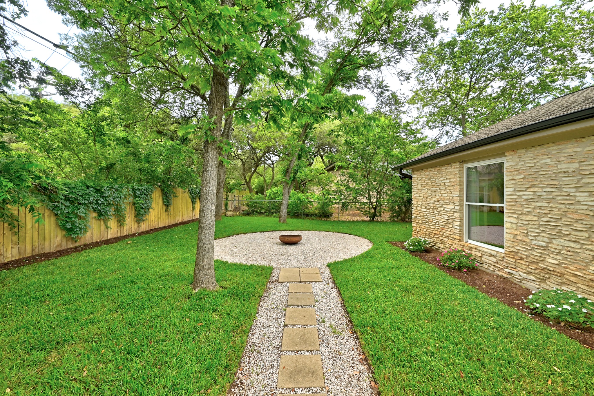 7110 Windrift Way Austin, TX 78745 - Photo 24 of 30 A well-maintained lawn with a stone path leads to a circular fire pit area, creating an inviting outdoor space.