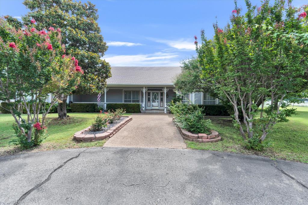 2717 Clear Lake Road Weatherford, TX 76087 - Photo 6 of 40 Ranch-style residence featuring a covered front porch with white columns, a concrete walkway, and landscaped garden beds