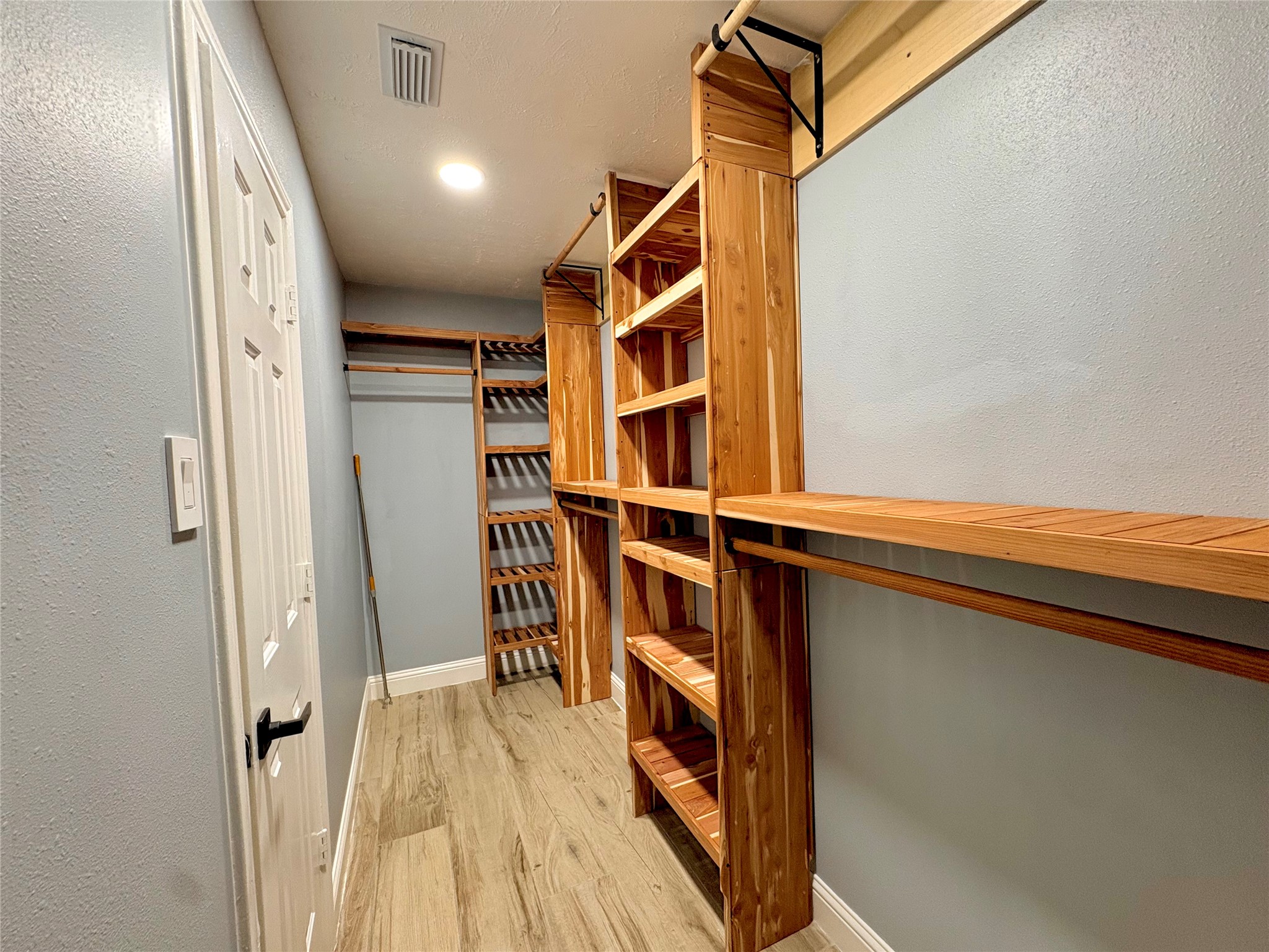 15410 Redbud Berry Way Cypress, TX 77433 - Photo 30 of 49 This photo shows a spacious walk-in closet with wooden shelving and hanging racks, providing ample storage. The room features light-colored walls and wood-style flooring, creating a warm and organized space.